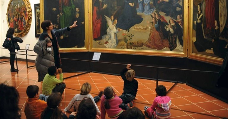 bambini seduti davanti al trittico Portinari del pittore fiammingo Hugo