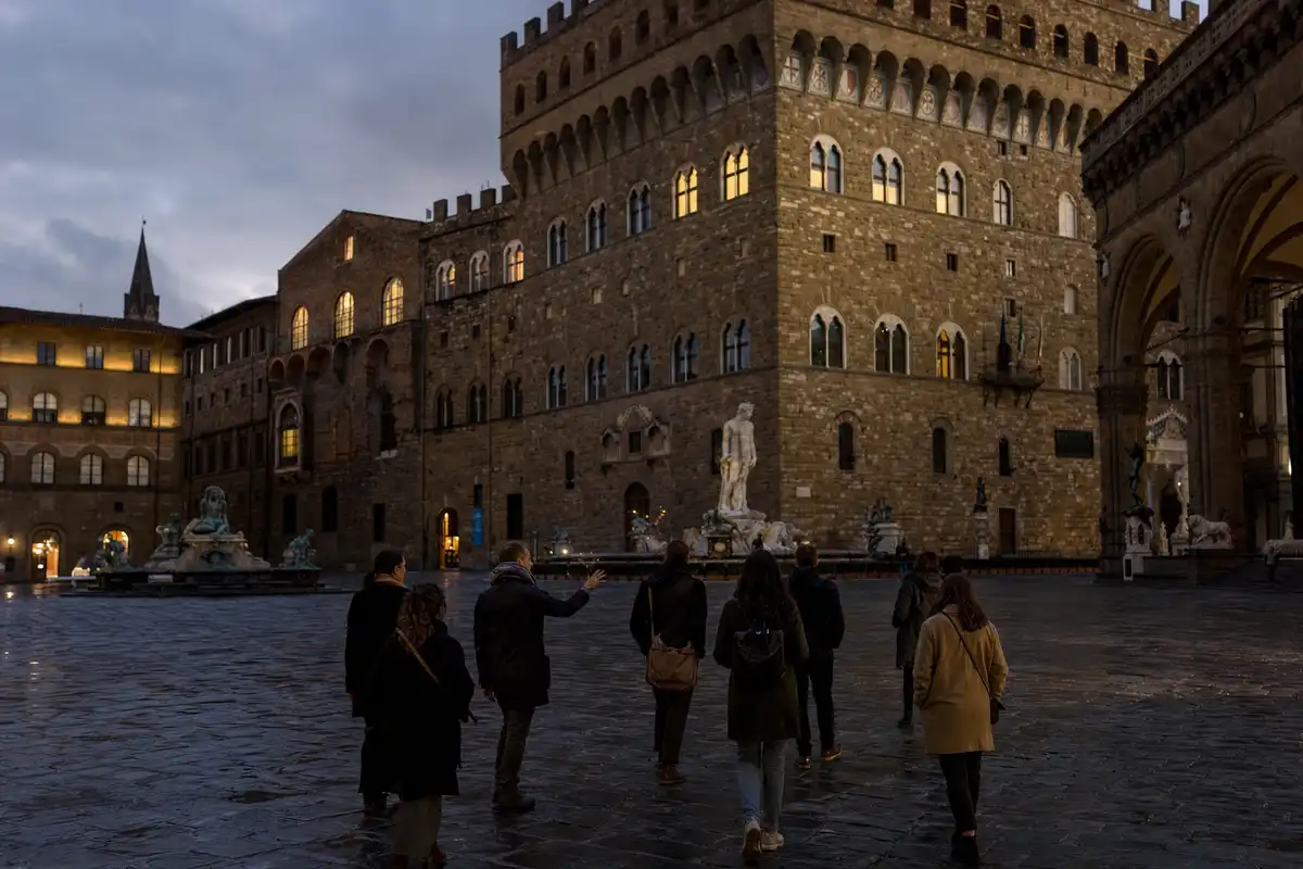 Visitatori al crepuscolo in Piazza della Signoria davanti a Palazzo Vecchio, con statue e luci serali