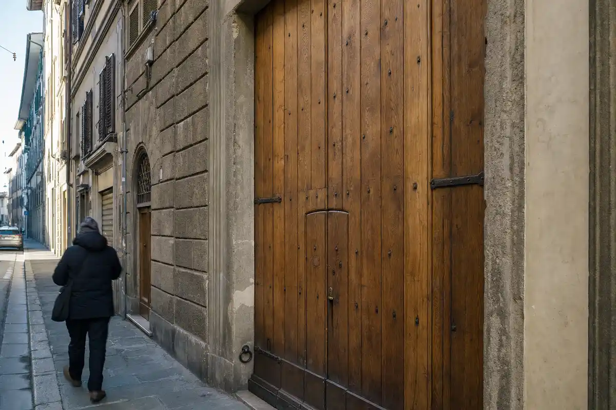 Grande portone in legno con porticina integrata su una strada di Firenze, con un passante sfocato