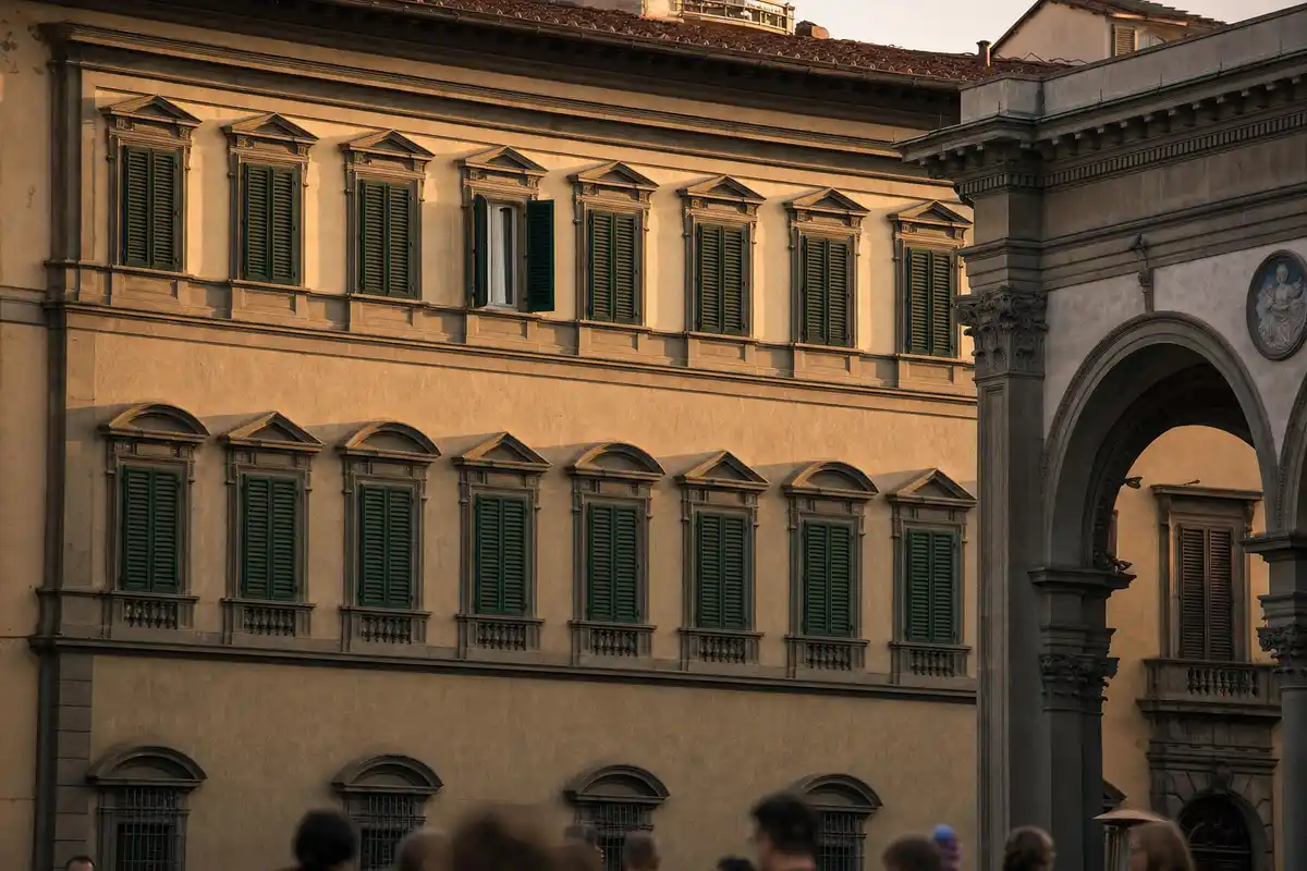 Facciata di un palazzo a Firenze con persiane verdi, una finestra al secondo piano socchiusa e portico ad arco a lato