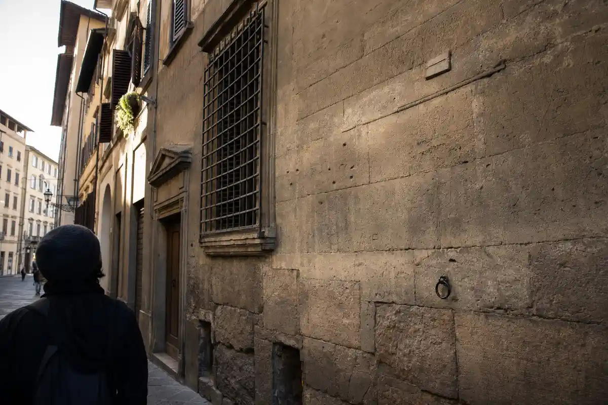 Persona di spalle in una via del centro di Firenze che guarda una targa alta su un muro in pietra